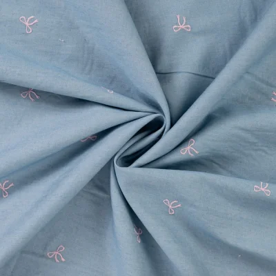 Tissu Chambray Coton brodé Noeuds roses sur fond Bleu denim - Par 10 cm